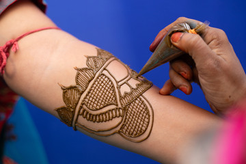 young woman mehendi artist painting henna on bride's hand before wedding day