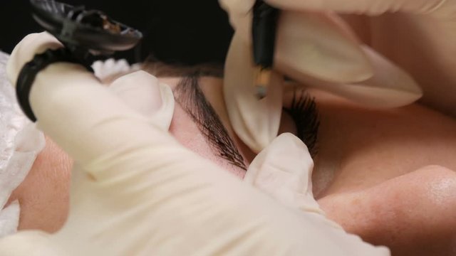 Microblading eyebrow tattoo, permanent makeup. A master in gloves, using special needle, injects pigment into the skin and stains the eyebrows using hair technique, making them natural, close-up view