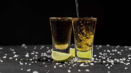 tequila is poured into two glasses on black background