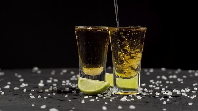 tequila is poured into two glasses on black background