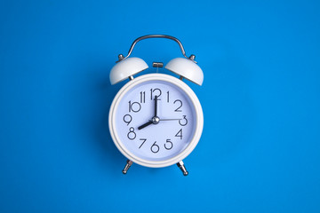 A white alarm clock on a blue background. a top view. a close-up picture representing 8 o'clock