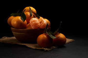 Fresh mandarin oranges fruit or tangerines with leaves on black table. Dark background.
