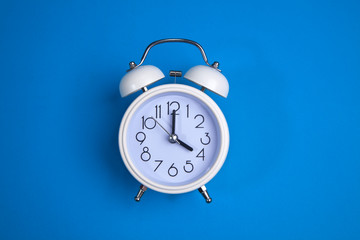 A white alarm clock on a blue background. a top view. a close-up picture representing 4 o'clock
