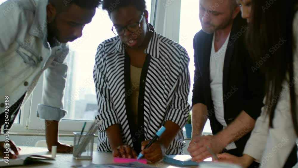 Poster diverse business team standing around meeting table in the office, discussing strategy and writing i