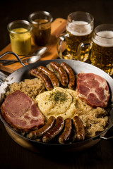 Sauerkraut Pfanne mit Nürnberger Rostbratwürste, Kassler Nacken,  Kartoffelpüree Senf und Bier auf Holz Tisch