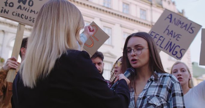 Back view of Caucasian female correspondent taking interview from a young pretty girl, social activist at the protest agains animals bad treating. Rear.