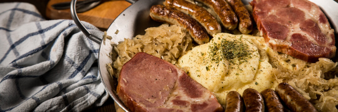 Sauerkraut Pfanne mit Nürnberger Rostbratwürste, Kassler Nacken,  Kartoffelpüree und Senf auf Holz Tisch