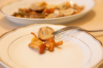 Mushrooms are small salty in sauce wet on a plate of white and sticks for eating 
