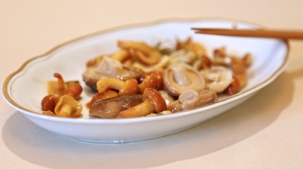 Mushrooms are small salty in sauce wet on a plate of white and sticks for eating 