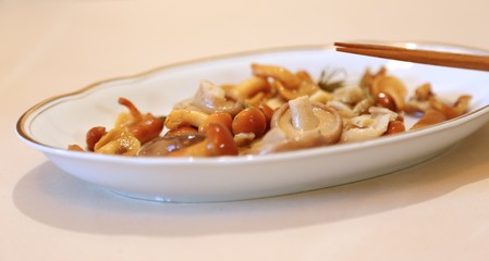 Mushrooms are small salty in sauce wet on a plate of white and sticks for eating 