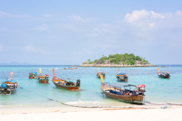 Fototapeta na wymiar Thai traditional longtail boats parked on a white sand beach surrounded by crystal clear turquoise water on a sunny, blue sky day on Thai paradise island of Ko Lipe, Thailand. Horizontal copy space