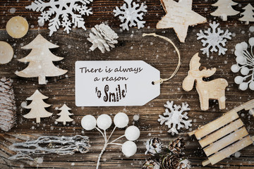 One White Label With English Quote There Is Always A Reason To Smile. Frame Of Christmas Decoration Like Tree, Sled, Star And Fir Cone. Wooden Background With Snowflakes