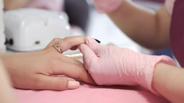 A manicurist wears the pink gloves. A table is white. The girl uses the manicure tools.