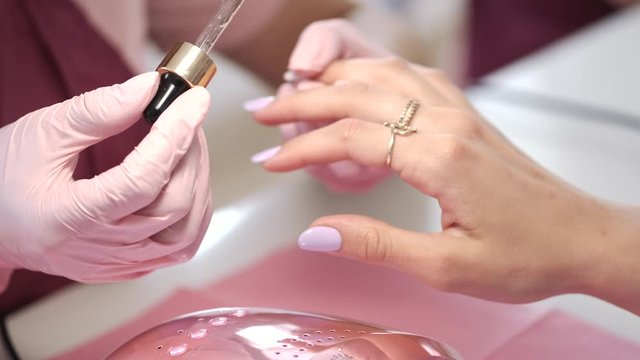 A manicurist wears the pink gloves. A table is white. The girl uses nail strip.