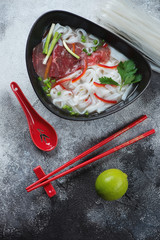 Bowl of pho bo soup with beef meat over grey stone background, vertical shot, flatlay