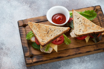 Sandwiches with grain bread, chicken fillet, cheese and vegetables on a rustic wooden serving tray, elevated view over beige stone background