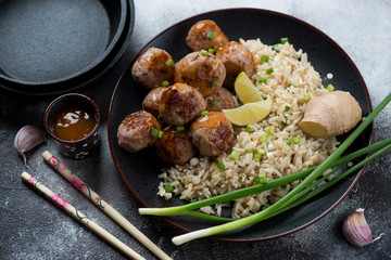 Black plate with pork meatballs and rice cooked in panasian style, studio shot over grey stone background