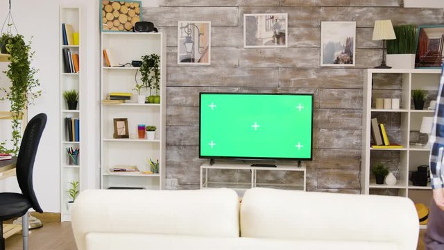 Back view of man sitting on sofa and watching a green screen tv