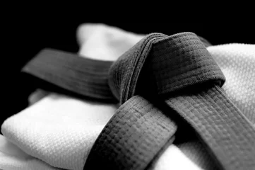 Foto op Plexiglas Black judo, aikido or karate belt on white budo gi. Concept is applicable to sports, business or education © marritch