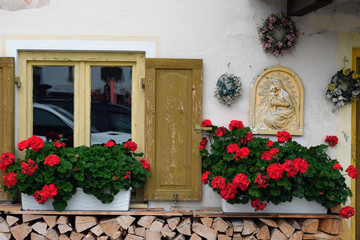 Fototapeta na wymiar window with shutters, geranium, firewood and christmas wreath
