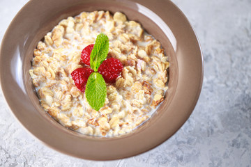 Healthy breakfast. Baked granola with milk and raspberries with mint in a plate. Tasty muesli, close-up