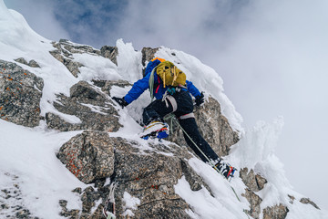 An alpinist climbing an alpine ridge in winter extreme conditions. Adventure ascent of alpine peak in snow and on rocks. Climber ascent to the summit. Winter ice and snow climbing in mountains.