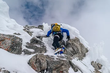 Foto op Canvas An alpinist climbing an alpine ridge in winter extreme conditions. Adventure ascent of alpine peak in snow and on rocks. Climber ascent to the summit. Winter ice and snow climbing in mountains. © Ondra