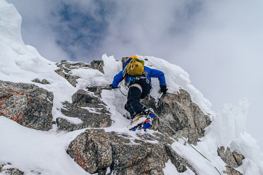 An alpinist climbing an alpine ridge in winter extreme conditions. Adventure ascent of alpine peak in snow and on rocks. Climber ascent to the summit. Winter ice and snow climbing in mountains.