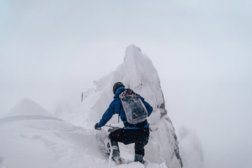 Fototapeta na wymiar An alpinist climbing an alpine ridge in winter extreme conditions. Adventure ascent of alpine peak in snow and on rocks. Climber ascent to the summit. Winter ice and snow climbing in mountains.