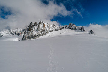 High alpine ridge in winter conditions. Rocky mountain ridge with ice and snow. Winter alpine landscape of Mount Blanc Massif, France. Blue sky and sunny day in high mountains.