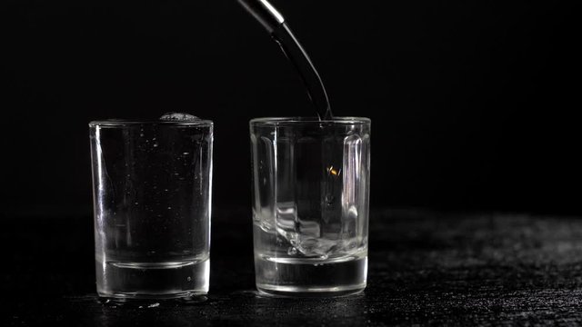 vodka is poured into two glasses on black background