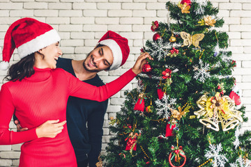 Romantic sweet couple in santa hats having fun decorating christmas tree and smiling while celebrating new year eve and enjoying spending time together in christmas time at home