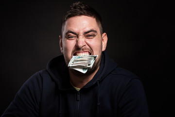 A young man with a bundle of money in his teeth. Close-up. Black background.