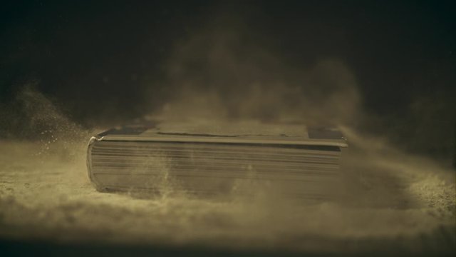 Super slow motion shot of a book falling down on a dusty wooden table, close-up