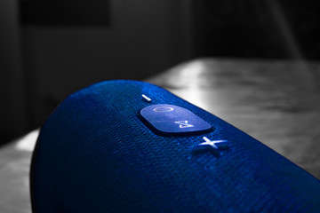 Wireless music column. Blue bluetooth speaker is on the table. Control and volume buttons.