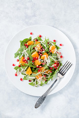 Fresh green organic salad with raw ingredients close up. Tasty salad with arugula, orange slices, pomegranate and cheese on white plate, top view. Healthy eating, dieting concept