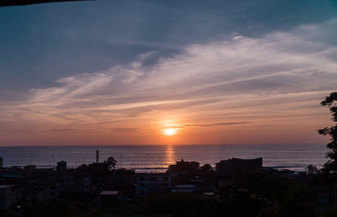 Man with sunset doing yoga. Tourist Man sitting and looking at beautiful orange, yellow and blue sunset over Montanita beach town from bamboo hut. Shot in Ecuador.