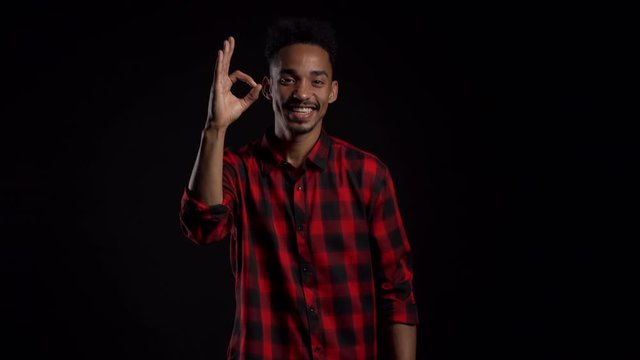 Handsome man in red wear on black studio background smiles to camera and gives ok sign. Happy african american guy showing gesture of approval. Winner.Success.