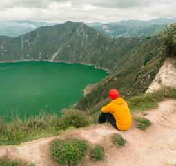 Woman at mountain volcano lake. Hiker in red looking at dramatic perspective of Quilotoa lake and crater view. Hiking loop from viewpoint. Shot in Ecuador. Green and blue. Freedom, Adventure © Jam Travels