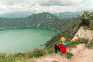 Woman at mountain volcano lake. Hiker in red looking at dramatic perspective of Quilotoa lake and crater view. Hiking loop from viewpoint. Shot in Ecuador. Green and blue. Freedom, Adventure.