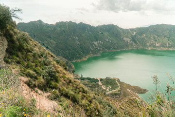 Obraz na płótnie Canvas Volcano crater lake view, Quilotoa. Dramatic perspective of Quilotoa lake and volcano crater, with view of mountains, hiking path trail loop and cloudy sky from viewpoint. Shot in Ecuador. Green blue