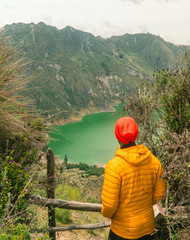Fototapeta na wymiar Woman at mountain volcano lake. Hiker in red looking at dramatic perspective of Quilotoa lake and crater view. Hiking loop from viewpoint. Shot in Ecuador. Green and blue. Freedom, Adventure