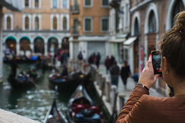Beautiful girl traveler photographs the streets and canals of Venice on her smartphone.