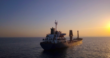 Obraz premium Large Cargo Ship facing Sunrise with flare.