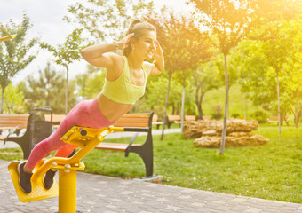 Attractive athletic woman doing exercises on exercise machines on the sports ground outdoors