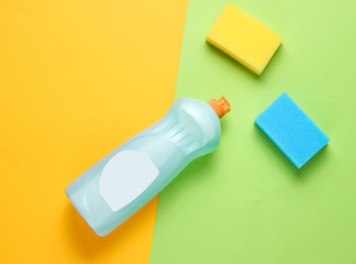 A bottle of detergent gel for dishes, sponges on a colored paper background. Top view