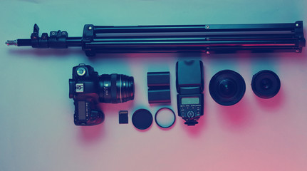 Fototapeta premium Equipment professional photographer. Camera, lenses, flashes, light filters, tripod. Neon light. Top view