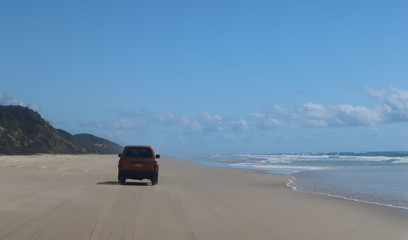 Fototapeta na wymiar Car driving on the beach close to the water