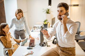 Confident businessman solving some business on the phone in the architectural bureau with colleagues on the background