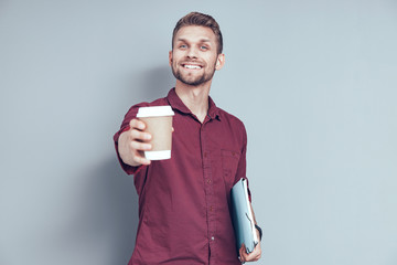 Happy young man is offering coffee in studio